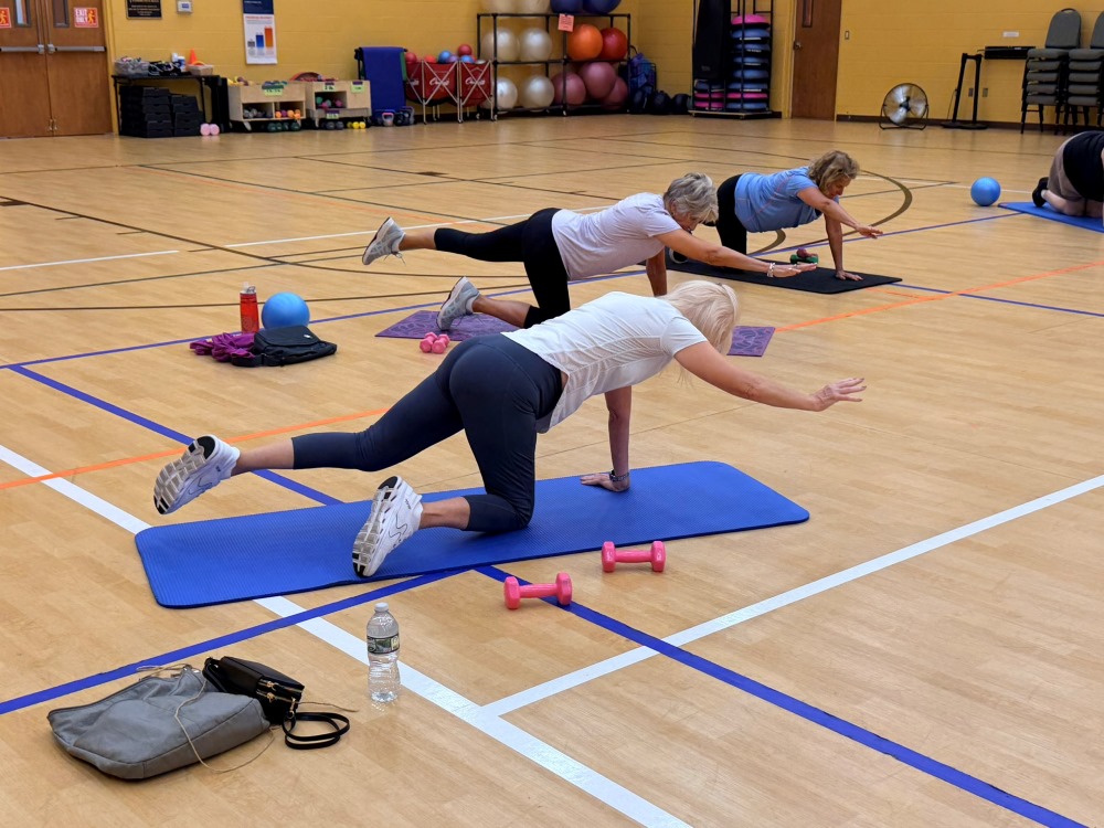 Multiple women stretching on a yoga mat on the ground with weights next to them